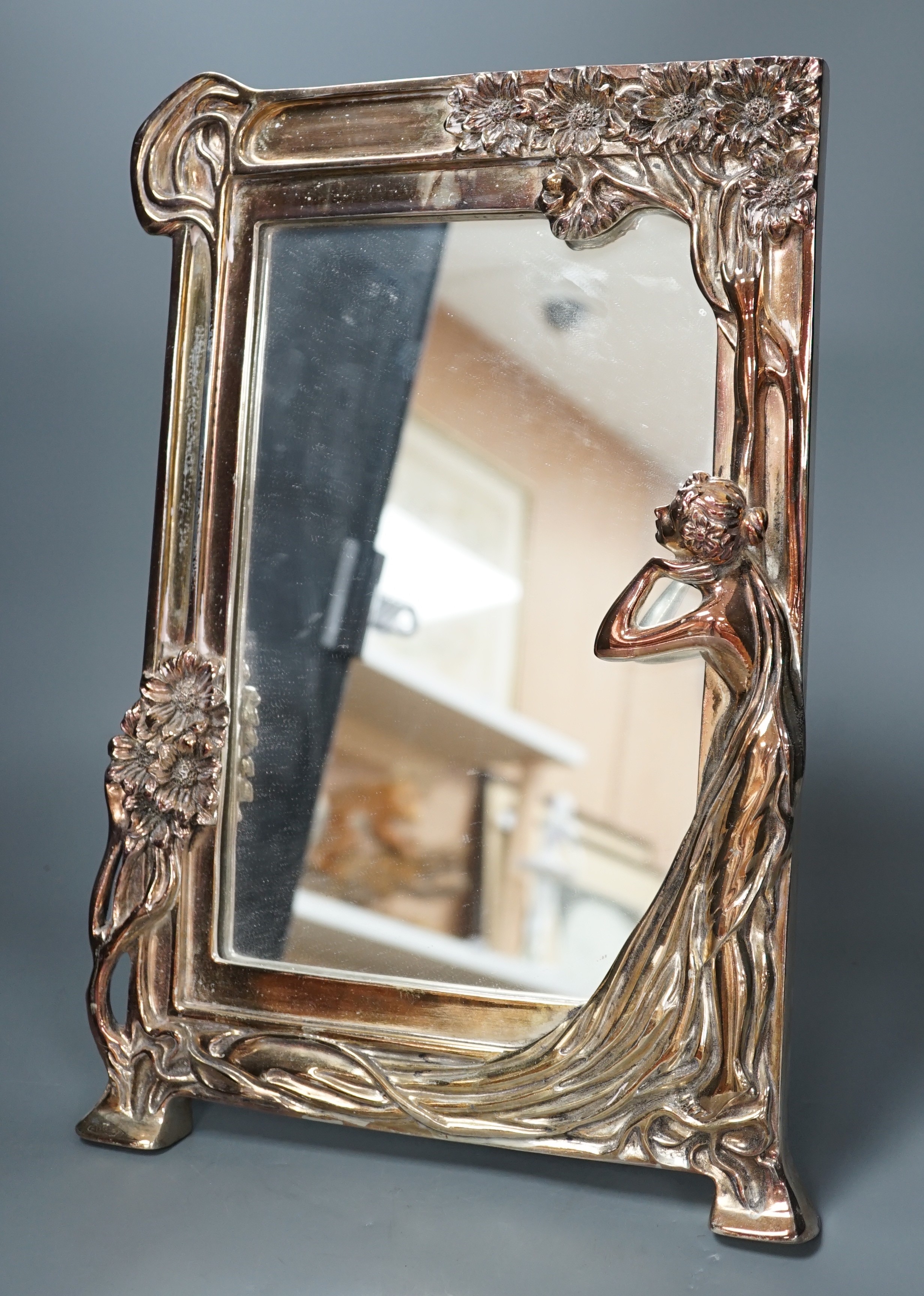 A silver plated Art Nouveau style mirrored frame, decorated with a female figure, tree and flowers in relief, 39.5cms high